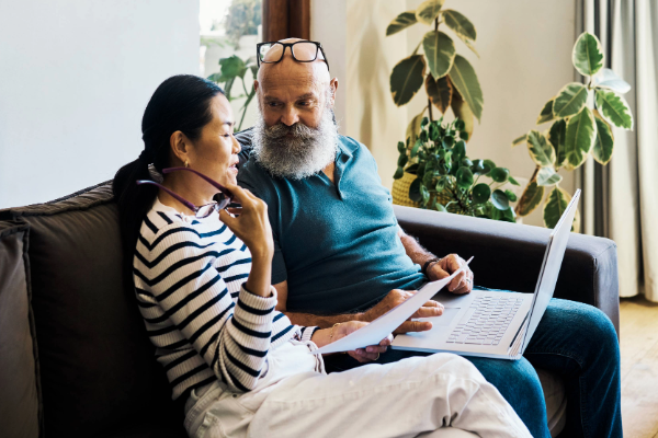 middle aged couple sitting on the couch looking at paper documents and a laptop